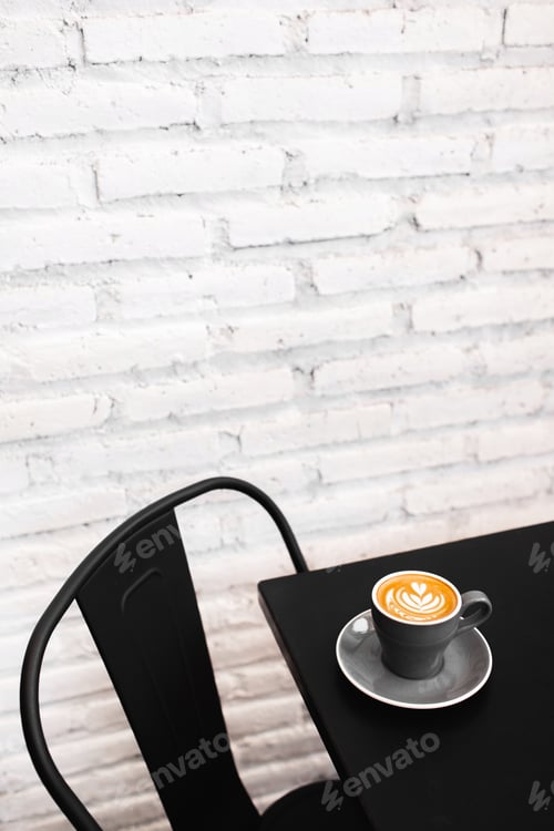 Preview: One gray cup of fresh cappuccino on black table. Background of white textured brick wall