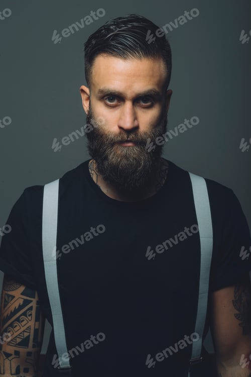 Preview: Portrait of young man with beard, wearing trouser braces, tattoos on arms