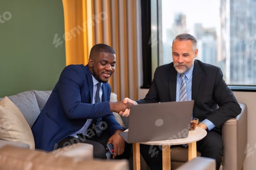 Preview: Two businessmen sitting on sofa working discuss on financial forecast together on laptop information