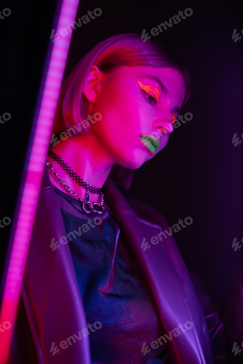 Preview: low angle view of woman with glowing makeup in purple neon light on dark background