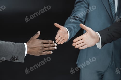 Preview: partial view of multiethnic group of businessmen outstretching hands for handshake isolated on black