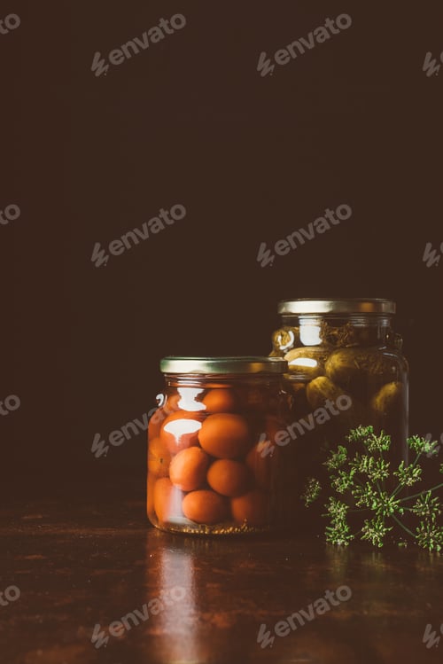 Preview: glass jars with preserved tomatoes and cucumbers on wooden table in dark kitchen