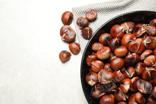 Preview: Delicious roasted edible chestnuts on light grey table, flat lay. Space for text