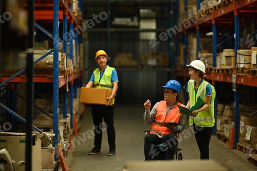 Preview: Man manager in wheelchair and young workers inspecting stock product in a large warehouse.