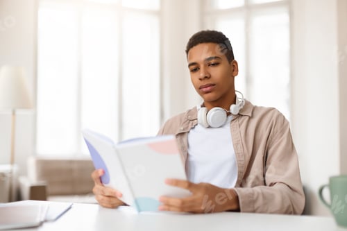 Preview: Young man reading a book with headphones