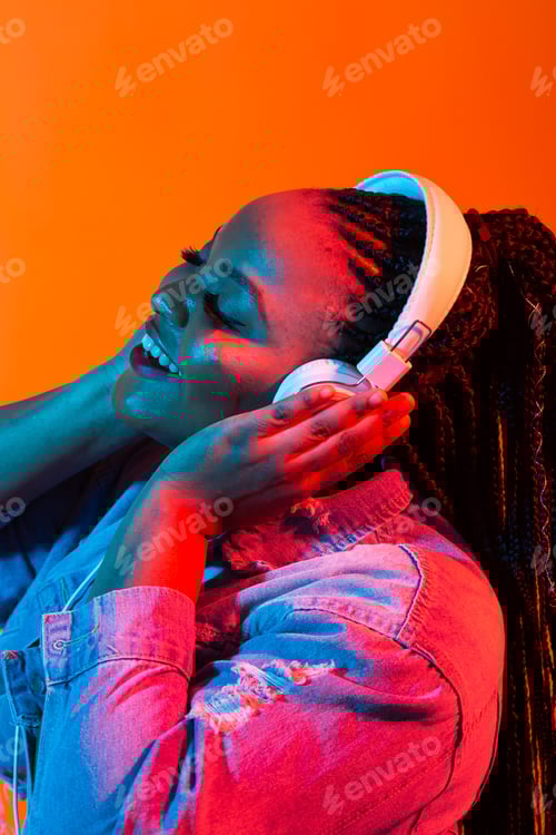 Preview: Young african-american woman listening to music in headphones in neon light. Female portrait