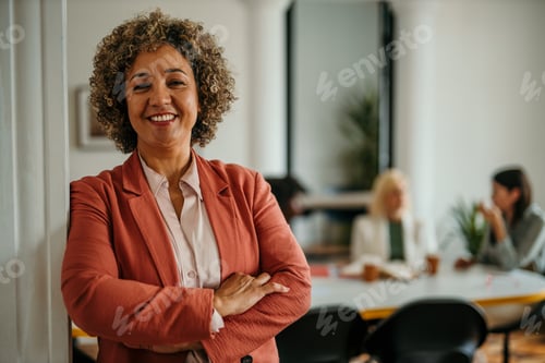 Preview: Smiling senior businesswoman posing in modern office with coworkers in background