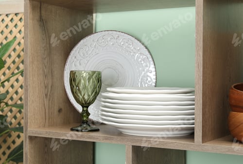 Preview: Different plates and glass on wooden shelf near green wall indoors