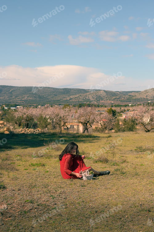 Preview: Woman wearing a red dress and holding a white basket with almond tree flowers