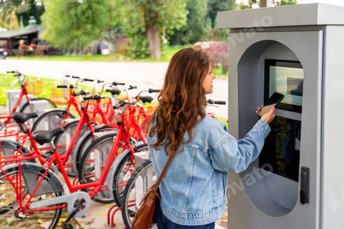 Preview: Woman using payment kiosk using payment kiosk at public bike share station for renting bike.