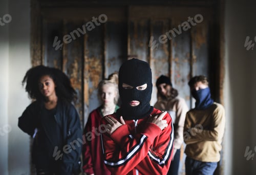 Preview: Boy with mask with teenagers gang indoors in abandoned building, showing finger gun gesture.