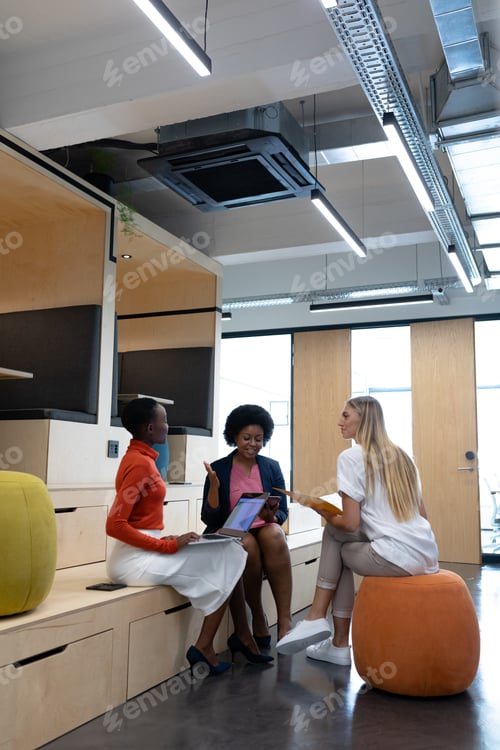 Preview: Diverse group of female business colleagues in discussion holding documents using tablet and laptop