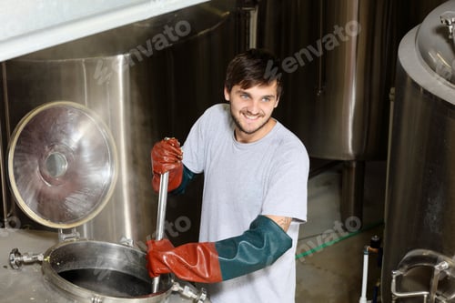 Preview: Worker in brewery, adding hops to brew kettle