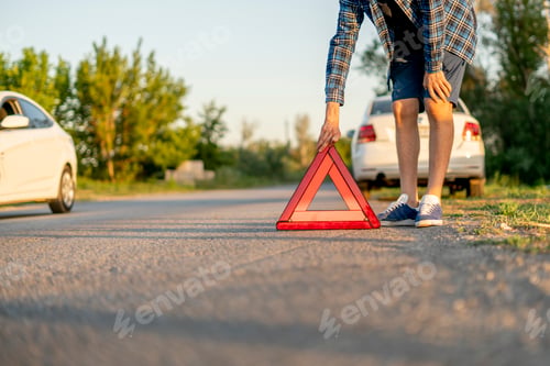Preview: a young man holding a red triangle and put it on the road, the sign of car accident