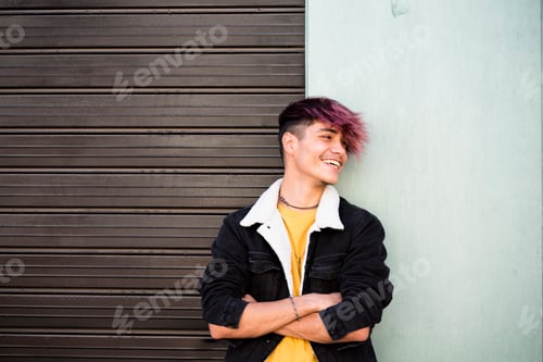 Preview: Teenage male with purple hair leaning on a vibrant colorful wall outdoors in a casual urban setting