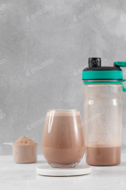 Preview: Chocolate protein shake with powder and shaker bottle on a light gray background