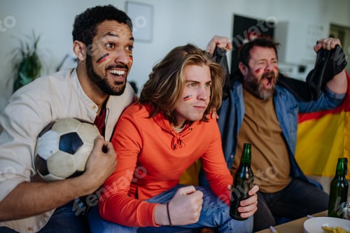 Preview: Happy German football fans friends watching football at home and celebrating