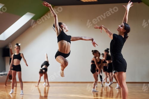 Preview: Woman teaching and helping. Group of female kids practicing athletic exercises together indoors