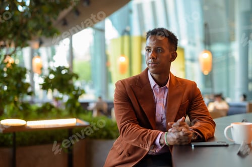 Preview: African businessman sitting in coffee shop using phone