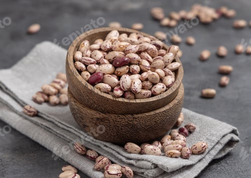 Preview: Wooden bowl full of dried pinto beans on napkin on gray closeup. Traditional Latin American legumes