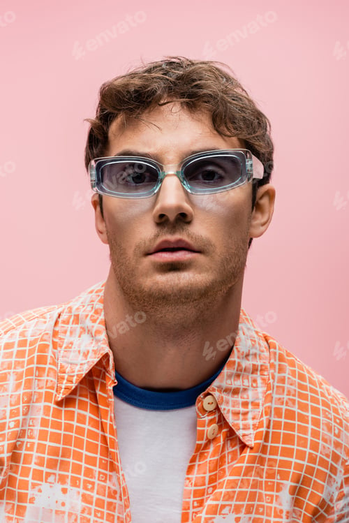 Preview: Portrait of brunette man in blue sunglasses looking at camera isolated on pink