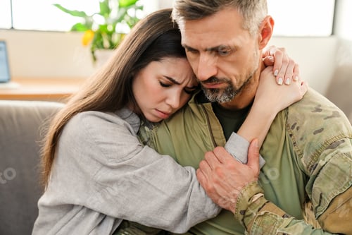 Preview: Unhappy woman hugging her military husband while sitting on sofa