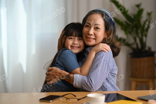 Preview: Affectionate grandmother cuddling her sweet lovely granddaughter and smiling at camera.