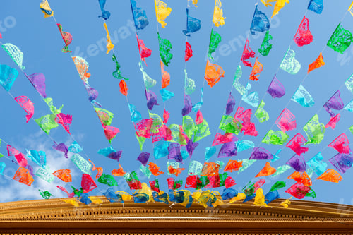 Preview: Colorful festive papel picado decorations hanging against the blue sky.