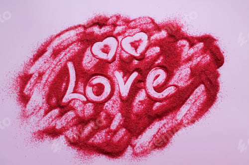Preview: The inscription Love is made on red sand. Two tiny hearts are drawn with a finger in the sand.