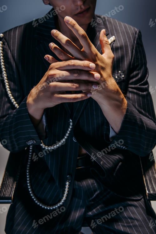 Preview: cropped view of stylish man in trendy suit with pearl chain gesturing on dark gray