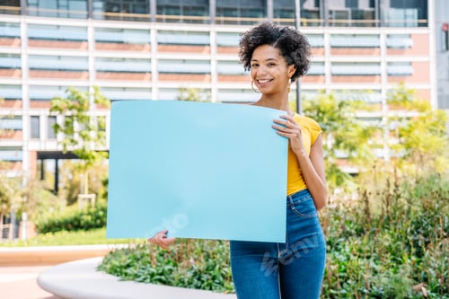 Visualização: Feliz jovem estudante de etnia demonstrando papel vazio no parque
