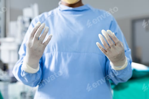 Preview: Midsection of surgeon wearing surgical gown and gloves in operating theatre