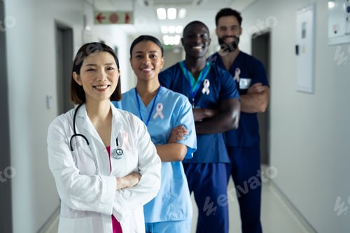 Preview: Portrait of diverse group of smiling healthcare workers wearing cancer ribbons standing in corridor