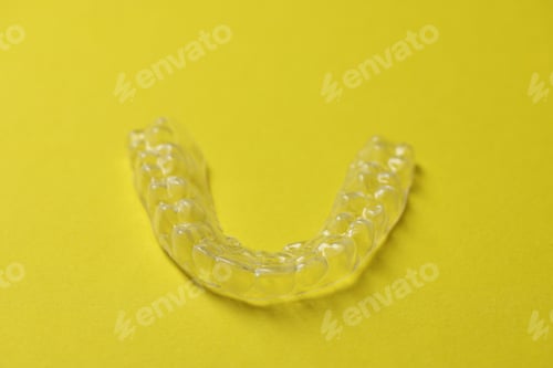 Preview: One clear aligner on yellow background, closeup