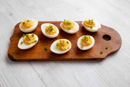 Preview: Homemade Deviled Eggs with Chives on a rustic wooden board on a white wooden table, low angle view.