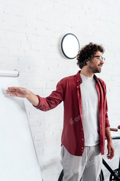 Preview: young man in eyeglasses pointing at whiteboard and looking away in office