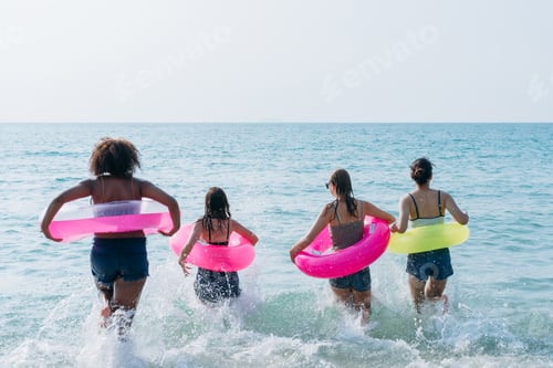 Preview: Teenagers laughing and playing in the sea with colorful swim rings, enjoying youthful summer fun.
