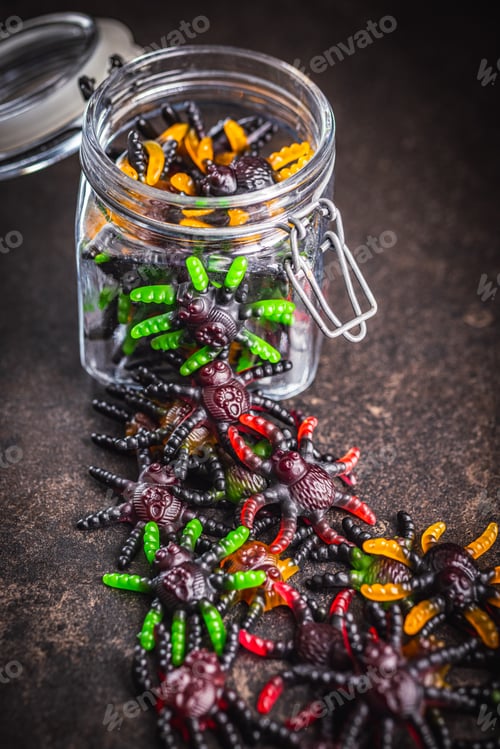Preview: Scary sweet jelly spiders. Halloween candies in jar on black table.