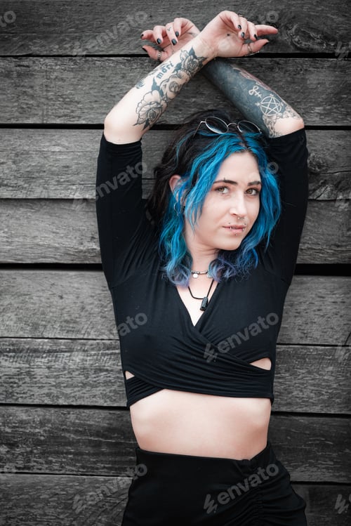 Preview: Young Caucasian female with blue hair standing against a wooden backdrop