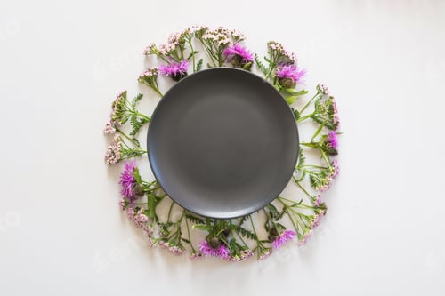 Preview: Wreath of wild purple and pink flowers on grey. Flat lay. View from above with space on black.