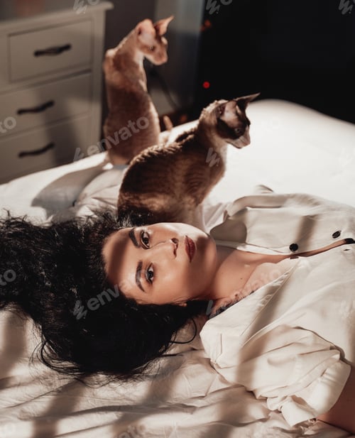 Preview: Brunette woman with curly hairs and cat lying on bed