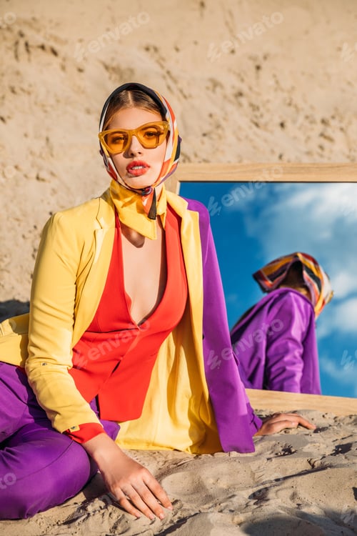 Preview: beautiful model in colorful fashionable clothes posing near mirror on sand dune