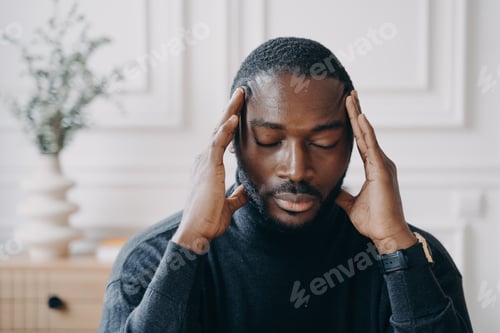 Preview: Exhausted young Afro American male entrepreneur sitting with eyes closed and with hands on his head