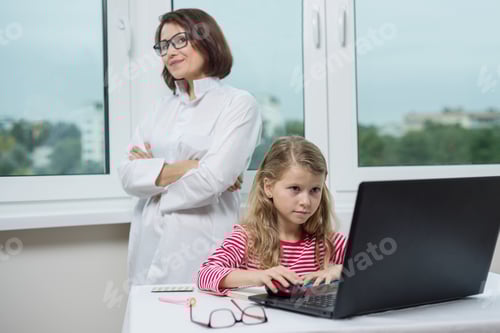 Preview: Child in office is sitting at table, looking at laptop, background of woman doctor