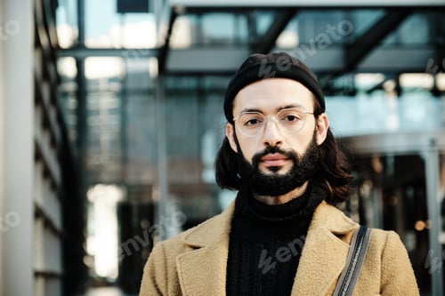Preview: Man looking at the camera with a serious expression while standing against an office building.