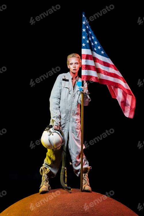 Preview: attractive female astronaut in spacesuit holding helmet and american flag on planet