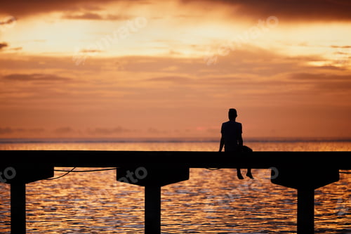 Preview: Man thinking on edge of pier at sunset