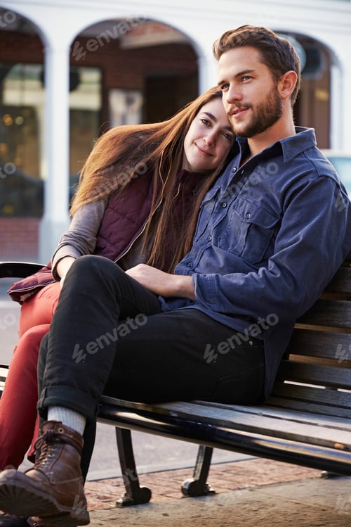 Preview: A young man and a young woman hugging, sitting on a bench in an urban environment.