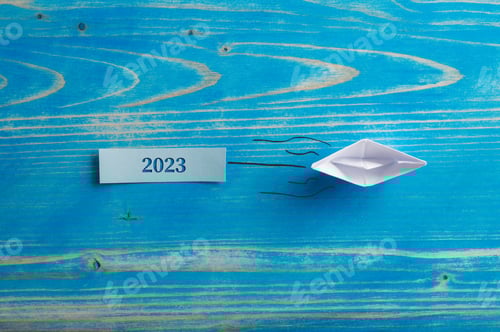 Preview: Origami made paper boat pulling a 2023 sign cut into a wooden plate