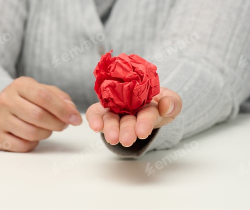 Preview: Female hand holds a crumpled red ball of paper.